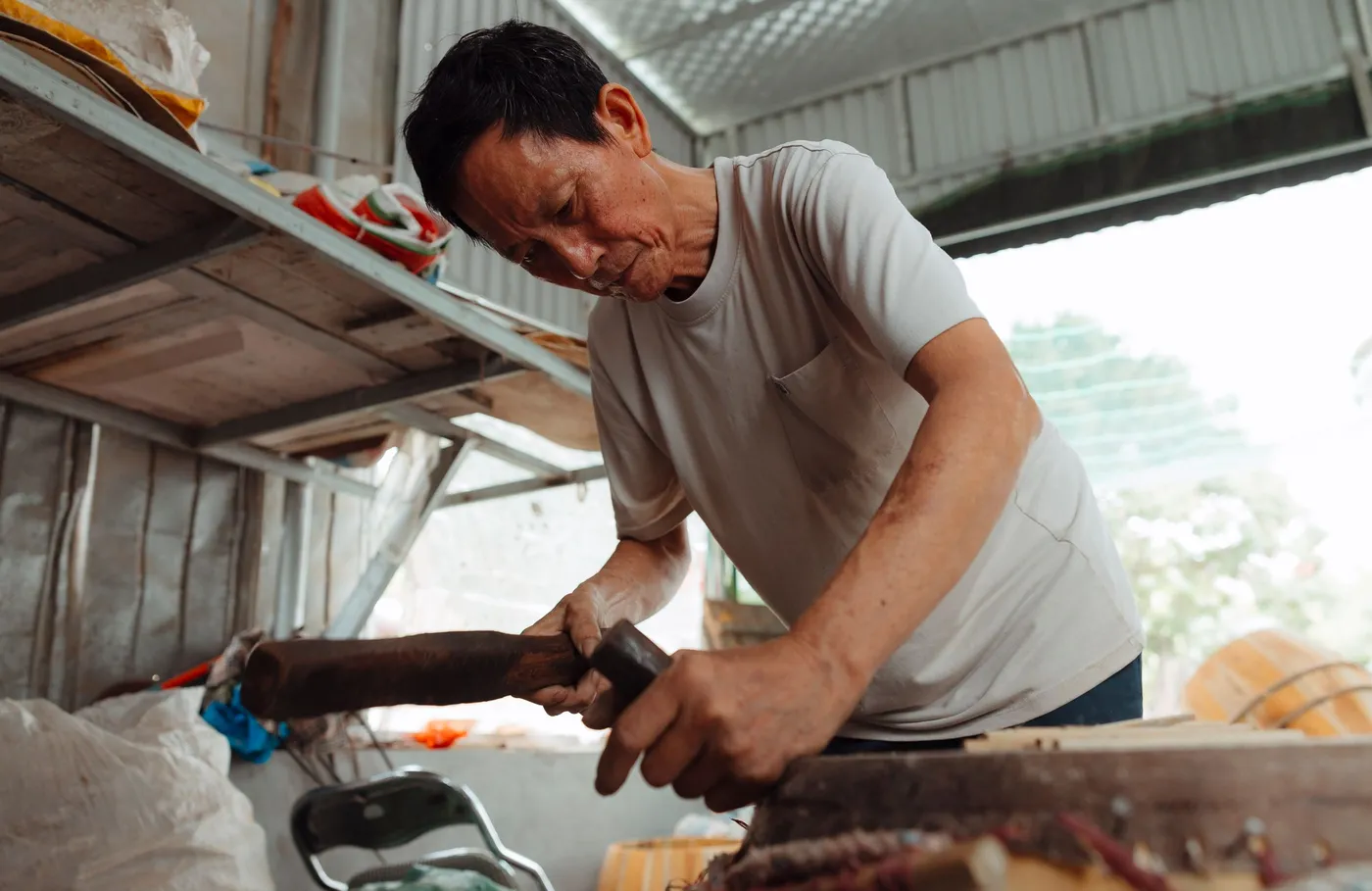 Thợ mộc lớn tuổi bào gỗ bên cửa xưởng